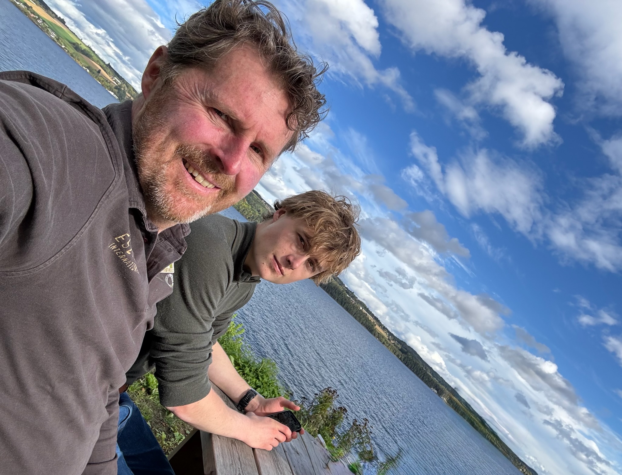 Selfie von Franz Hölzl und seinem Sohn Franz Martin an einem Holzgeländer über einem See, darüber blauer Himmel mit Wolken